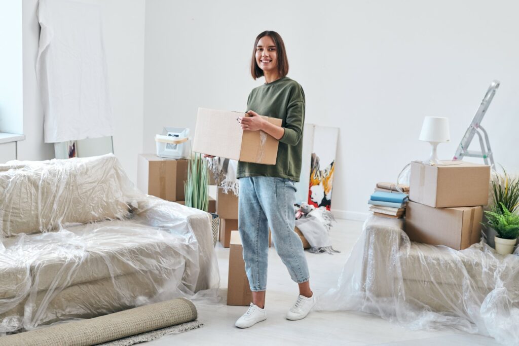 cheerful-young-woman-in-jeans-and-sweatshirt-carrying-packed-box